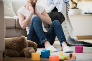 Overwhelmed exhausted woman feeling tired of cleaning in her messy house sitting on the floor with toys and laundry lying around her